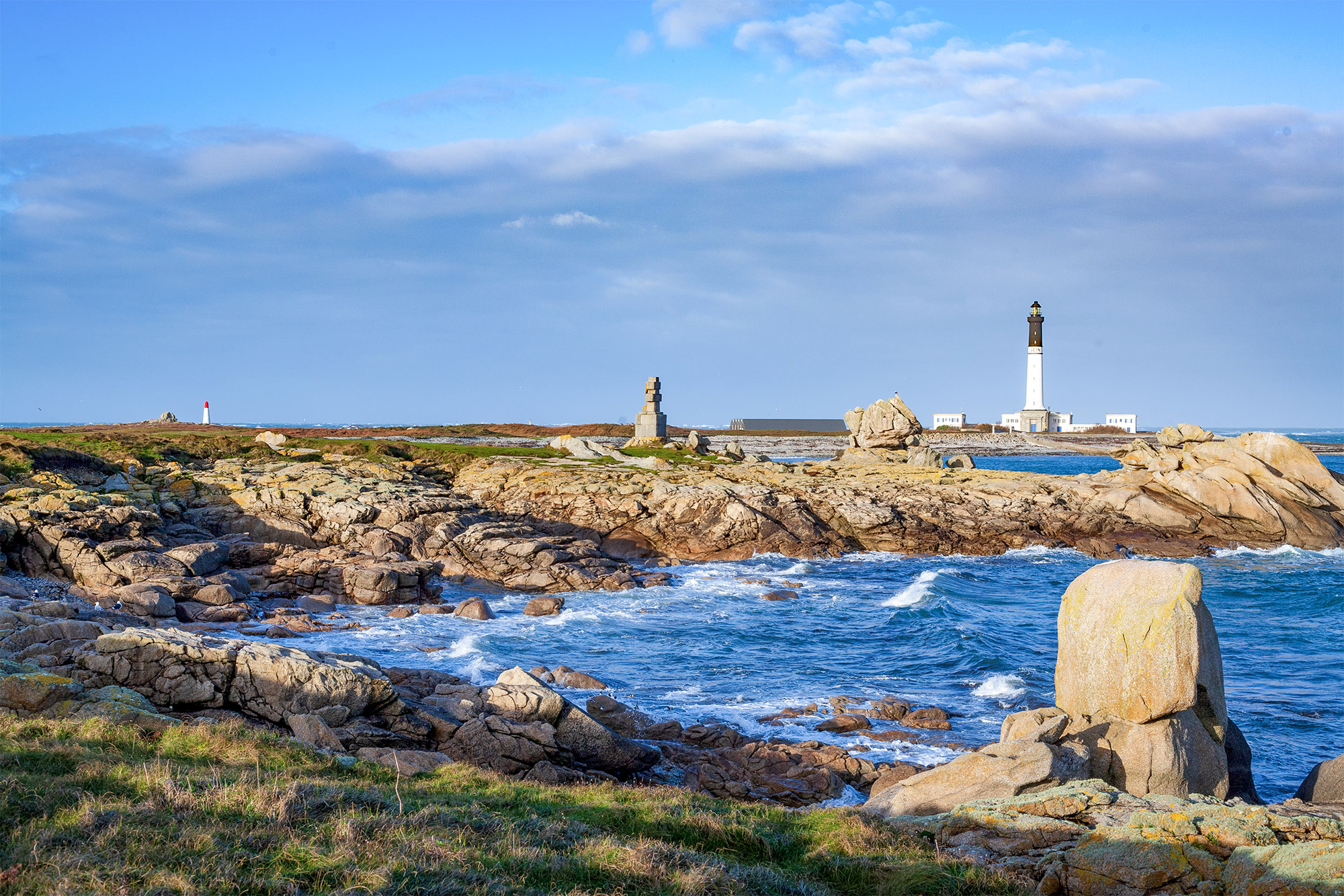 Phare sur côte rocheuse ensoleillée, ciel bleu.